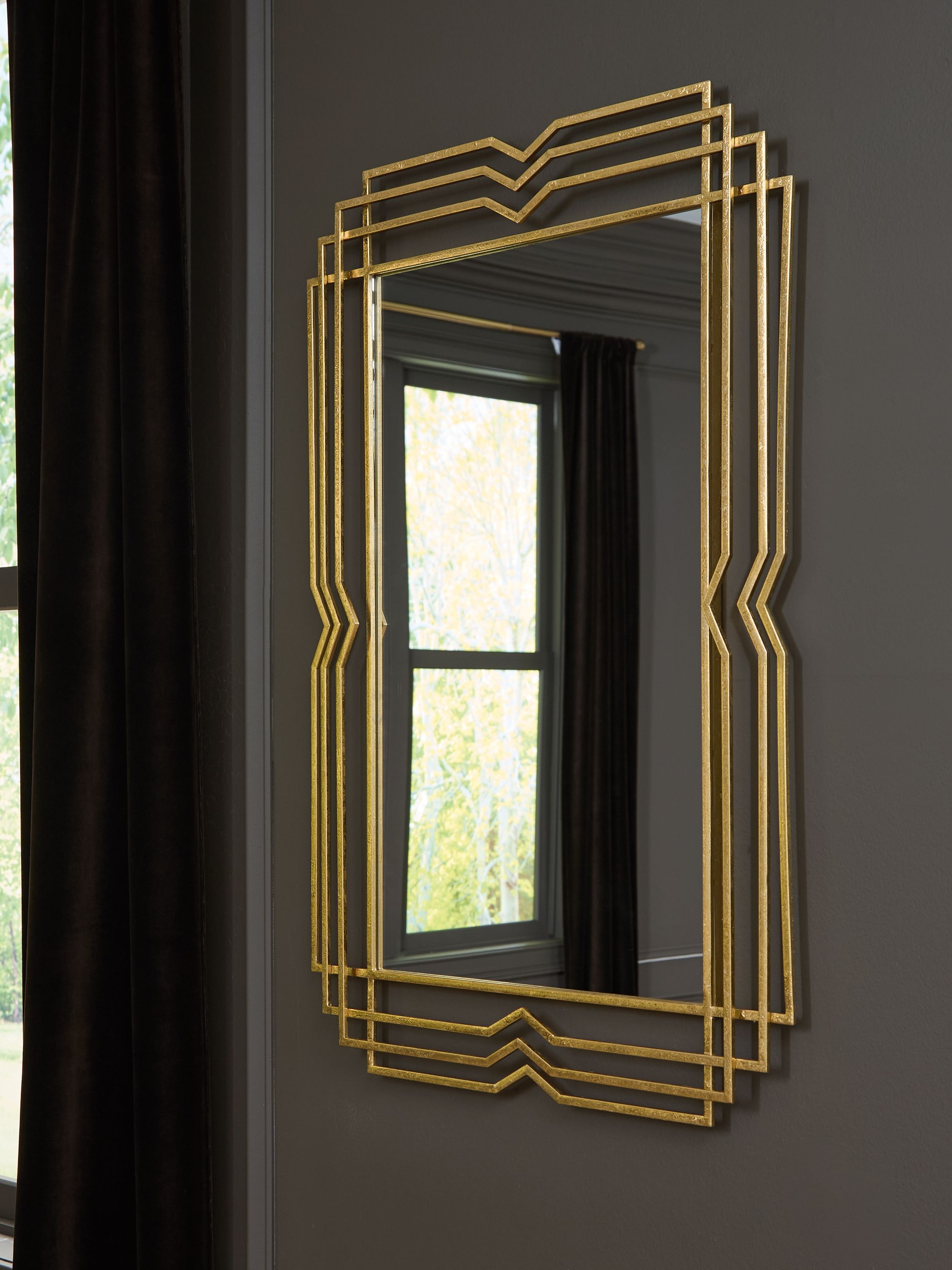 Gold layered-frame mirror hung on a dark charcoal wall beside a curtained window
