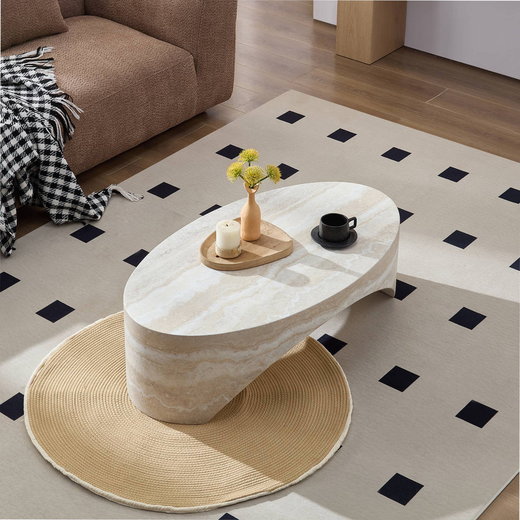 High angle perspective of the oval white marble coffee table styled on a contemporary black-and-white geometric rug next to a plush brown bouclé sofa.
