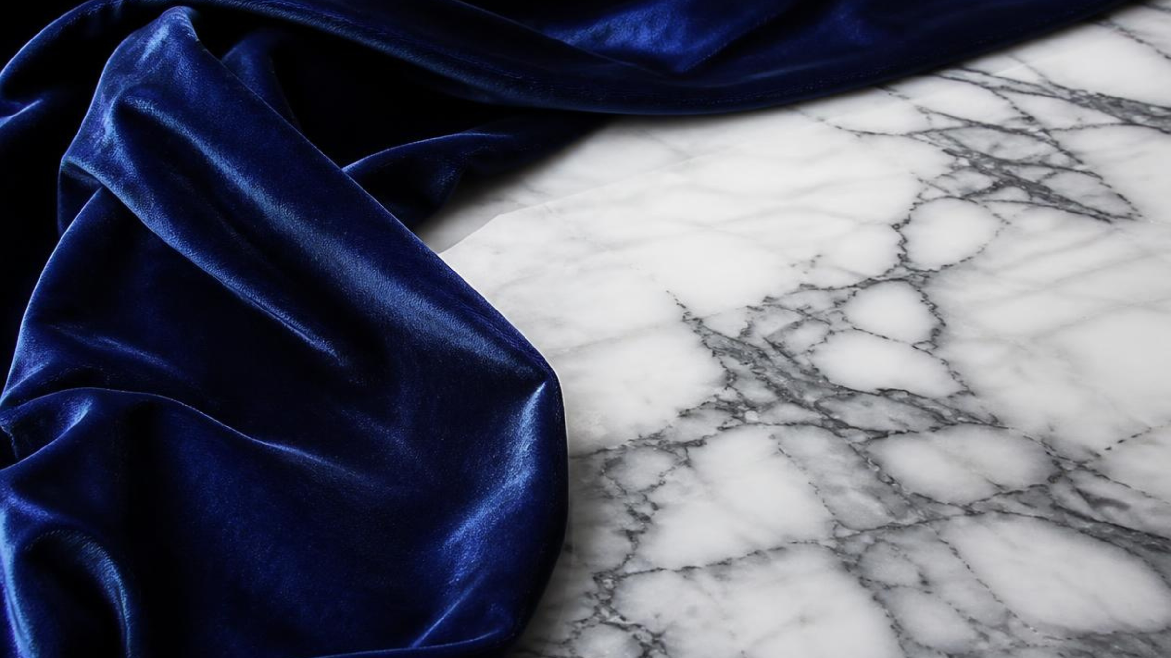 Deep sapphire velvet draped across white marble with dark mineral veining.