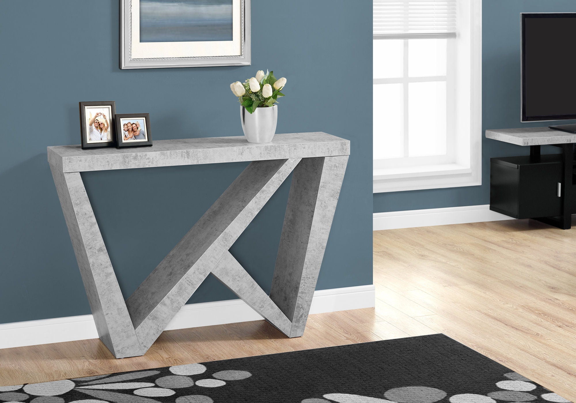 Dark gray console table with asymmetrical wedge base, styled with framed photos and a floral arrangement against a blue wall