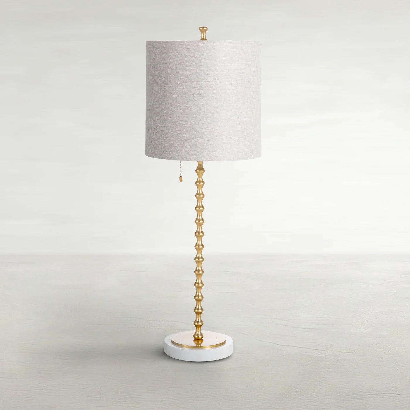 Full view of the Adèle Table Lamp with a cylindrical linen shade, segmented warm-gold stem, and round white marble base.