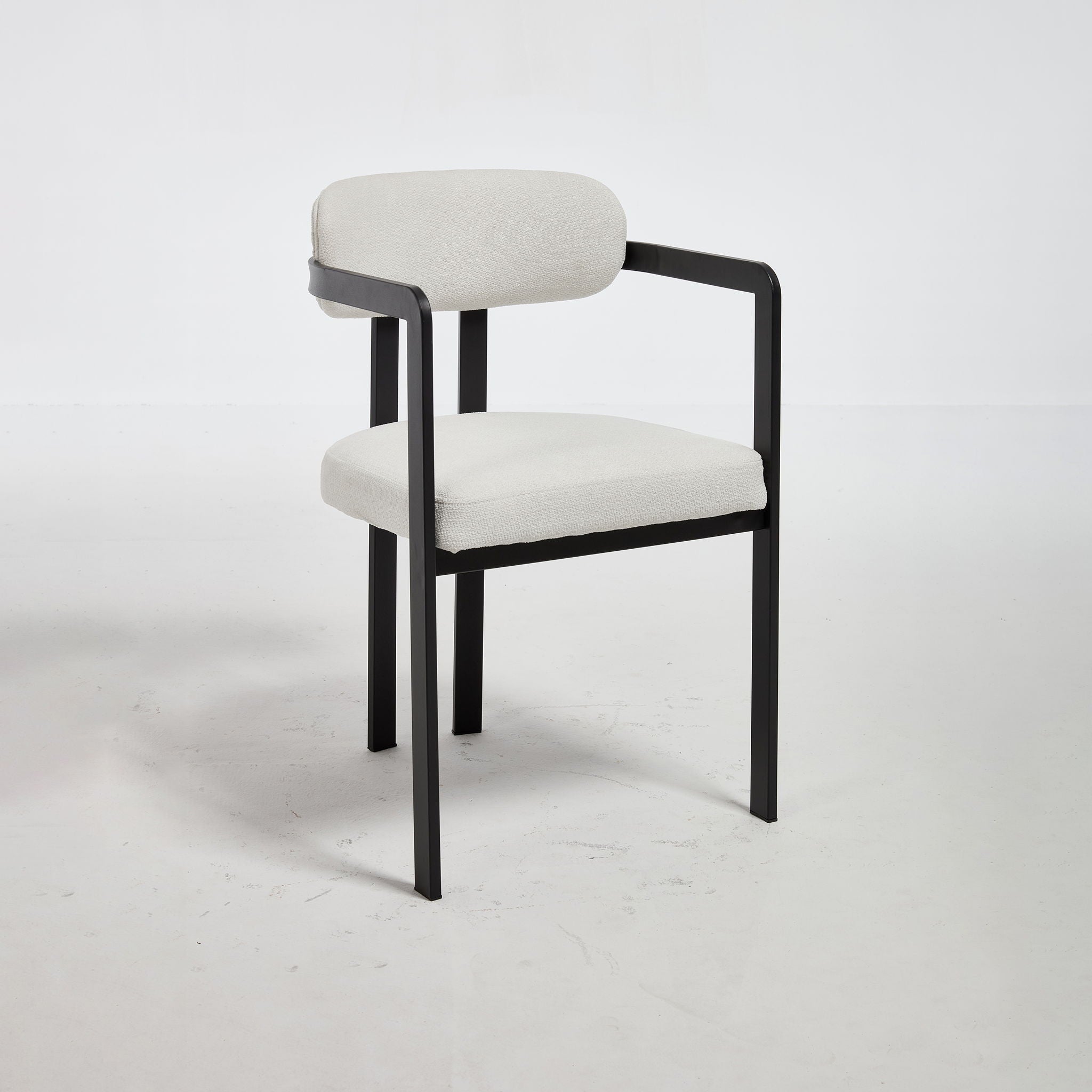 Symmetrical three-quarter studio view of the Helix dining arm chair in a crisp cream tailored textile, showcasing its minimalist matte black metal frame and track arms against a white background.