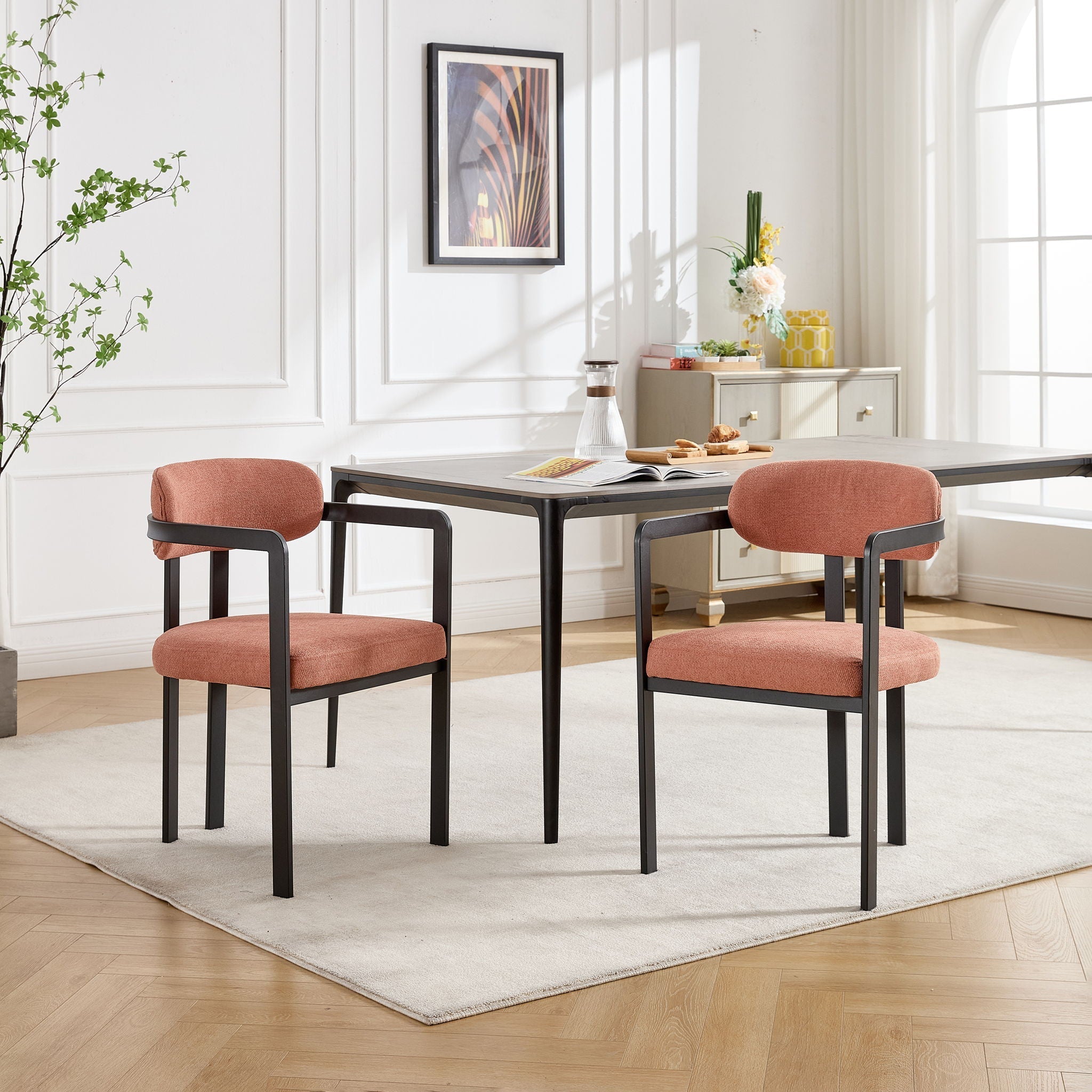 Editorial dining room view featuring a matching pair of Helix dining chairs in terracotta orange fabric, styled around a dark minimal wood table on a cream rug with an abstract framed art piece in the background.