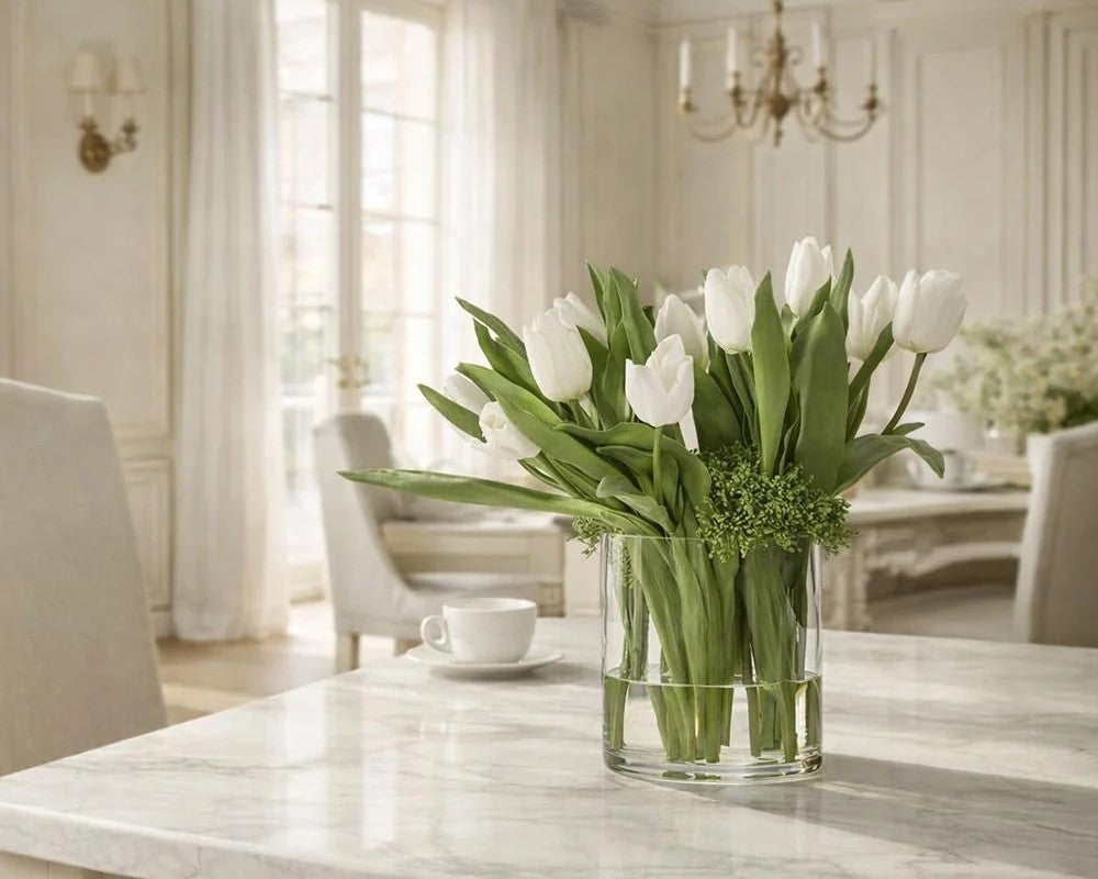 The Inès Tulip Arrangement centered on a pale dining table in a light neutral room, showing its upright tulip-and-foliage silhouette at room scale.