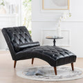Left-facing lifestyle room presentation of the Luca tufted black leather chaise lounge, emphasizing its fluid aerodynamic S-curve silhouette and tapered walnut legs.