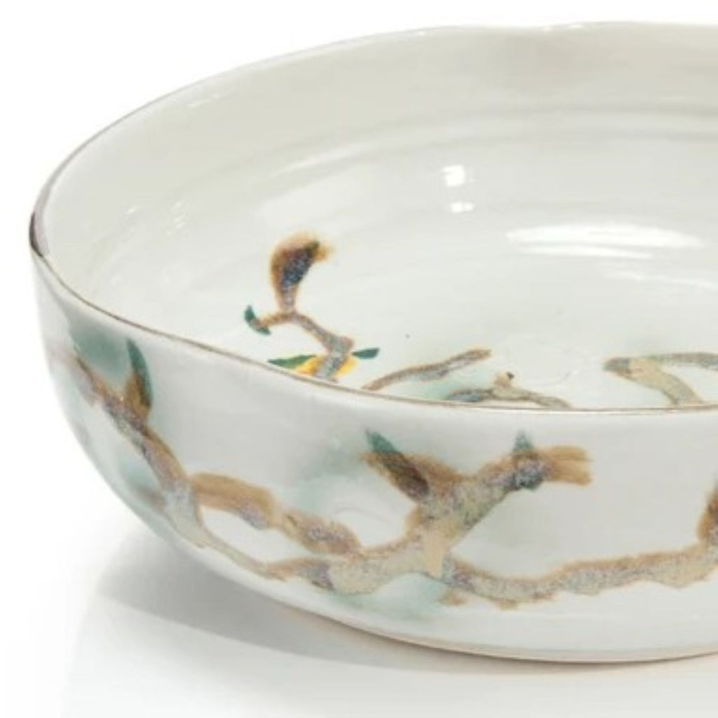 Close side view of the Nadine Bowl highlighting its softly irregular rim, glossy ivory glaze, and painted branch motif wrapping around the exterior.