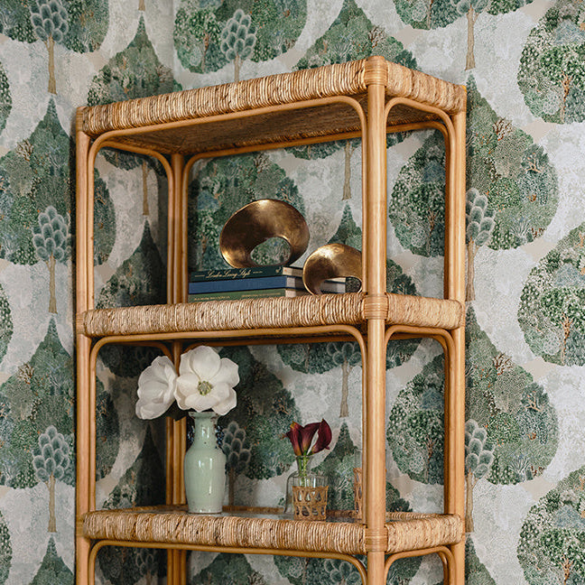Ruben sculptures styled on an open woven shelf against botanical wallpaper, showing the warm metal finish within a layered decorative arrangement.