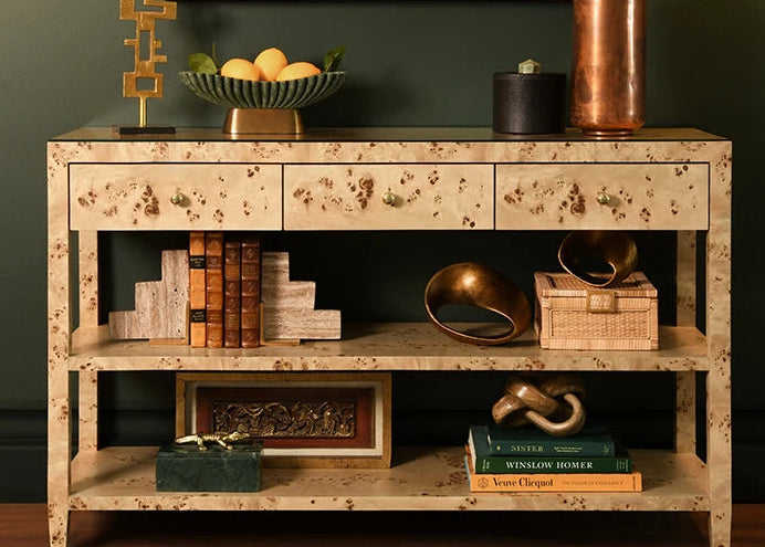 Ruben sculptures arranged on the lower shelf of a pale console in a dark green interior with books, metallic accents, and layered objects