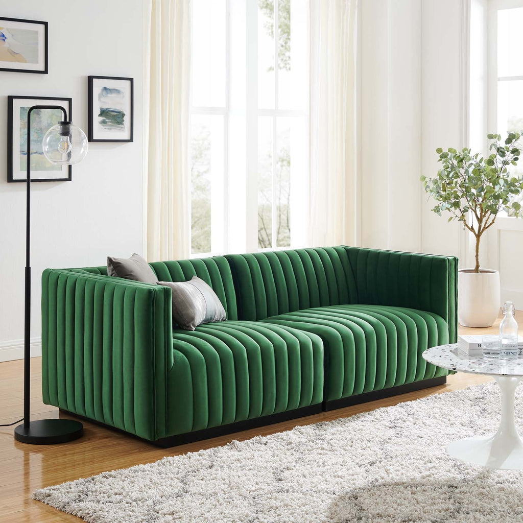 Editorial living room presentation of the Velvet Rogue modular loveseat in emerald green velvet, styled on a plush white shag rug next to a modern black floor lamp and a white tulip coffee table.